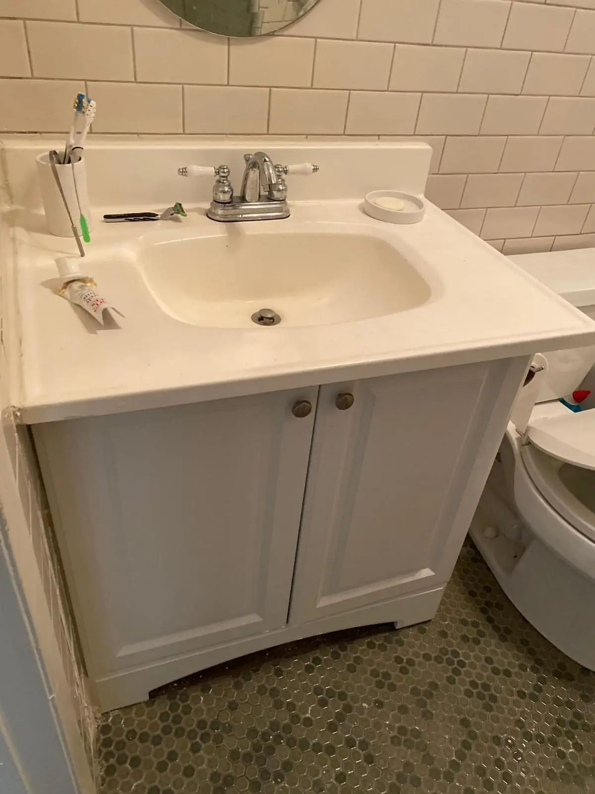 White vanity cabinet with an integrated sink and a chrome two-handle faucet, with subway tile behind it and a hexagon tile floor